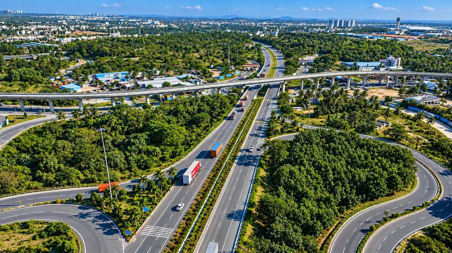 Aerial view of a highway interchange with an elevated metro line, trucks and dense greenery near Bengaluru