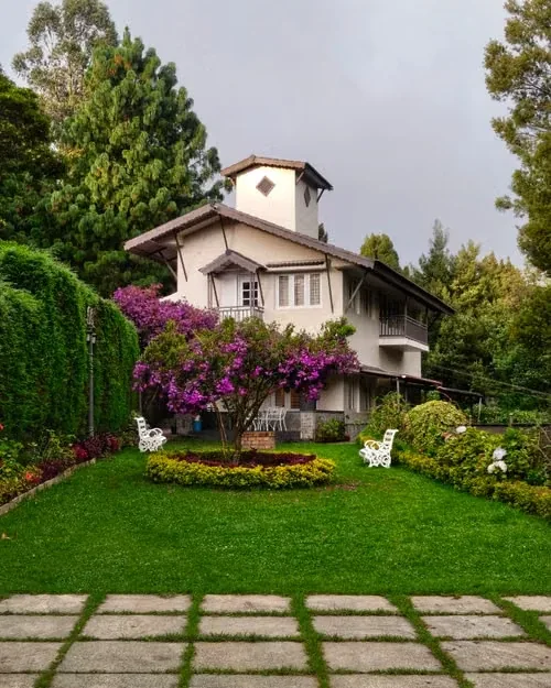 A hill-station style villa with a lawn, flowering trees and a stone path